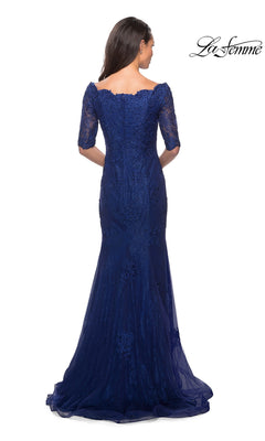 A woman is shown from the back wearing the Long Formal Dress: La Femme 26943—a floor-length, navy blue gown with elbow-length sleeves. This elegant mother-of-the-bride dress features a fitted silhouette and a small train, highlighted by delicate lace and rhinestone accents.