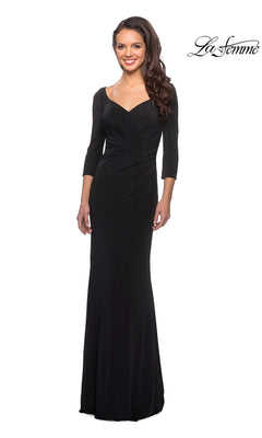 A woman stands and smiles against a white background, wearing the La Femme 26955 long formal dress. This modest gown features three-quarter length sleeves and a fitted sheath skirt that accentuates a form-fitting silhouette, while the slight sweetheart neckline lends an elegant touch.