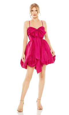 A woman wears the Short Party Dress 27040 by Mac Duggal, featuring a bright pink balloon hem, large chest bow detail, thin shoulder straps, and paired with nude high-heeled sandals.