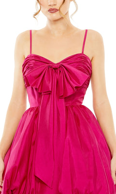 A woman wears the Short Party Dress 27040 by Mac Duggal, featuring a sleeveless, bright pink balloon hem, thin straps, and a large bow detail on the bodice.