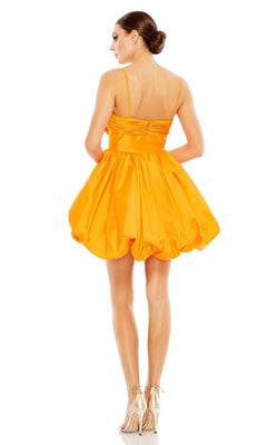 A woman faces away, wearing the vibrant orange Mac Duggal Short Party Dress 27040 with a sleeveless mini balloon hem and beige high heels against a white background.