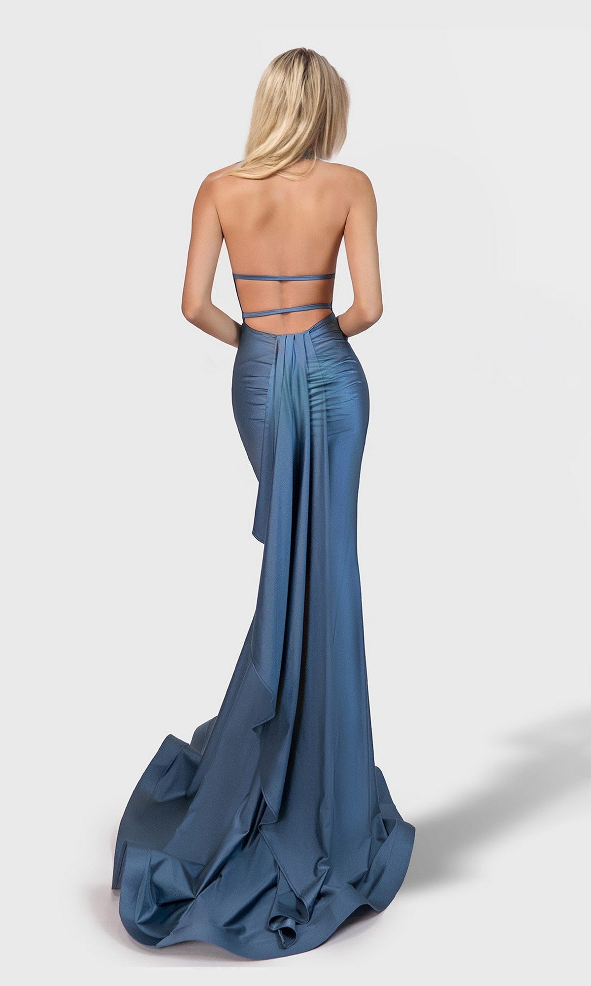A woman with long blonde hair models the Jessica Angel 2711, a fitted, strapless, backless sheath prom dress in blue satin with a floor-length flowing train, standing against a plain light background.