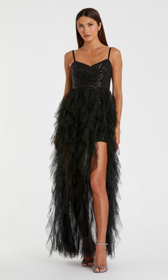 A woman wears the Mac Duggal 27119 Overskirt Mini Sequin Prom Dress—black, short, with a ruffled tulle skirt and high slit. Facing forward in silver heels, she flaunts the sparkling dress’s modern elegance.
