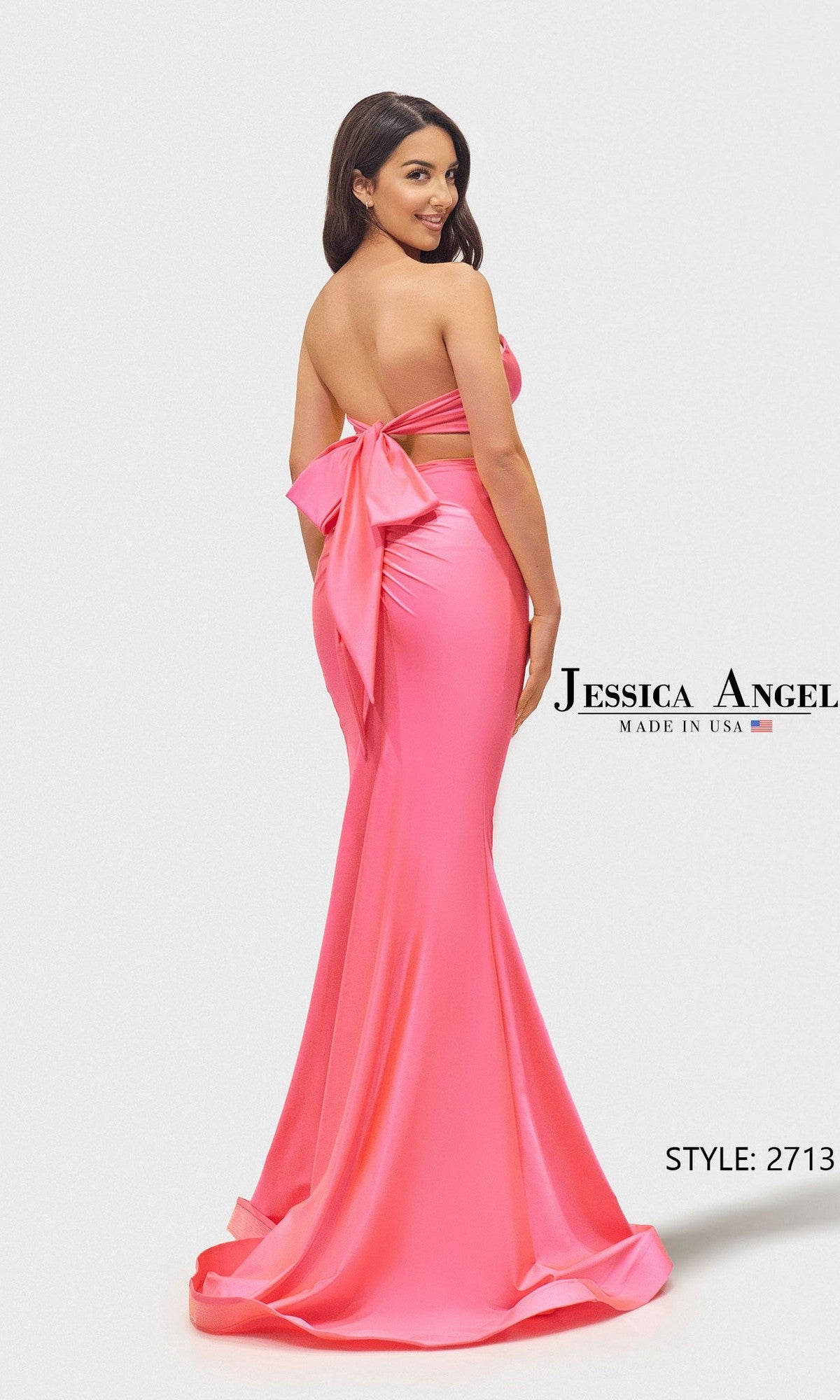 A woman models the Long Prom Dress: Jessica Angel 2713 in bright pink, striking a pose before a white background. The strapless gown stands out with its dramatic large back bow detail.