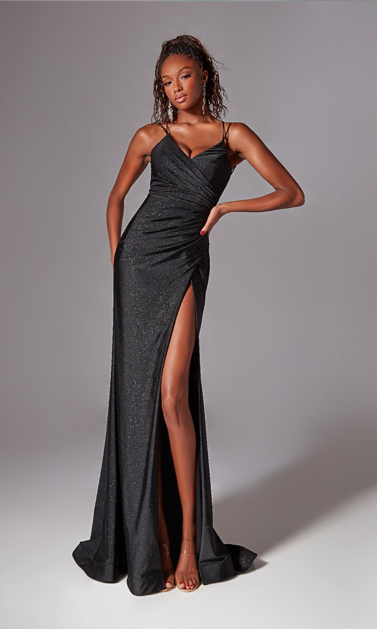 A woman poses with one hand on her hip against a neutral background, wearing the Lace-Up Long Glitter Prom Dress: Aerie Couture 271—a fitted black formal dress with thin straps and a high slit.