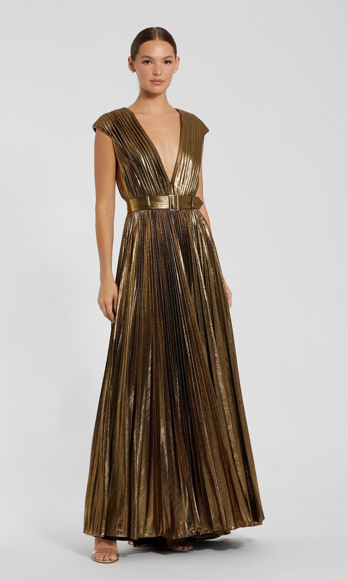A woman wears the Mac Duggal 27215 Pleated Long Bronze Evening Gown, featuring a floor-length pleated design, deep V-neckline, cap sleeves, and matching belt, set against a plain light background.