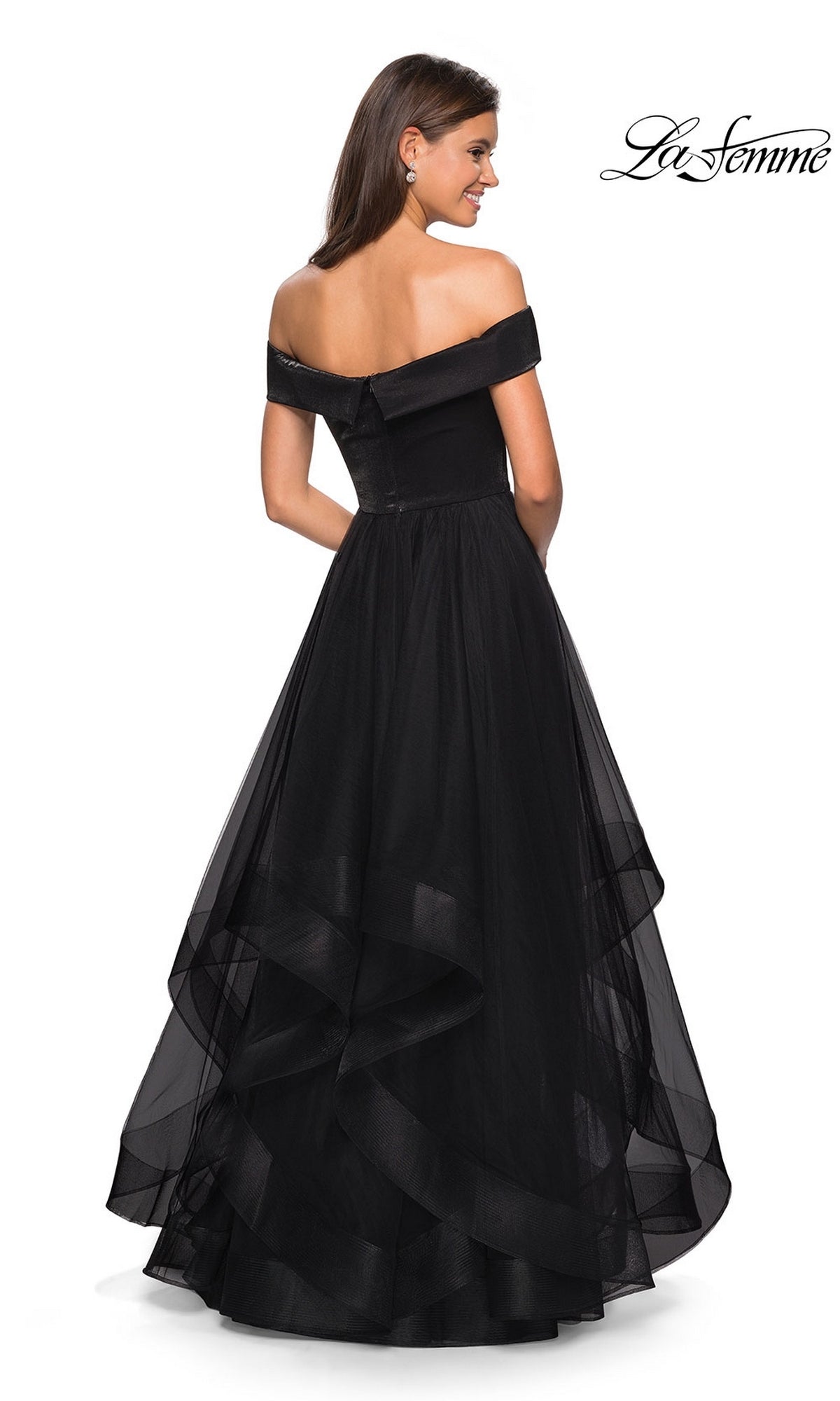 A woman stands smiling in the La Femme Off-Shoulder Long Tiered Prom Dress 27224, a stunning ball gown with a full tulle skirt, photographed from behind. The La Femme logo is visible in the top right corner.
