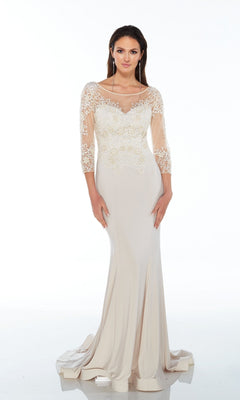 A woman wears the Long Formal Dress: Alyce 27257—a modest, elegant champagne evening gown with lace bodice and sleeves, and a sheer neckline.
