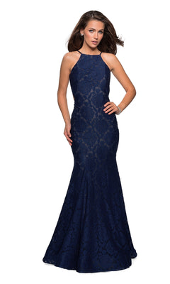 A woman poses against a white background in the La Femme Floral Lace Mermaid Prom Dress 27289, featuring a sleeveless, navy blue design with a high neckline, fitted silhouette, and floor-length floral lace.