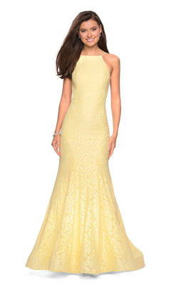 Woman wearing the La Femme Floral Lace Mermaid Prom Dress 27289—a sleeveless, floor-length pale yellow gown with floral lace and a high neckline—standing and smiling with her hands by her sides.