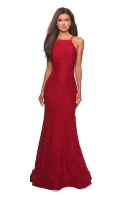 A woman models the La Femme Floral Lace Mermaid Prom Dress 27289, a sleeveless, fitted, floor-length gown with a high neckline and open low V-back, against a plain white background.