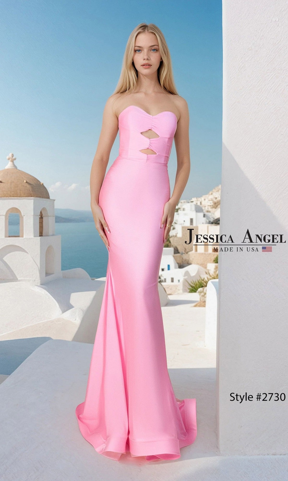 Woman wearing the Jessica Angel 2730 Long Prom Dress in Bubblegum, a strapless, form-fitting satin-jersey gown with cutout details. She stands on a white terrace overlooking blue sea and white buildings. Text: 
