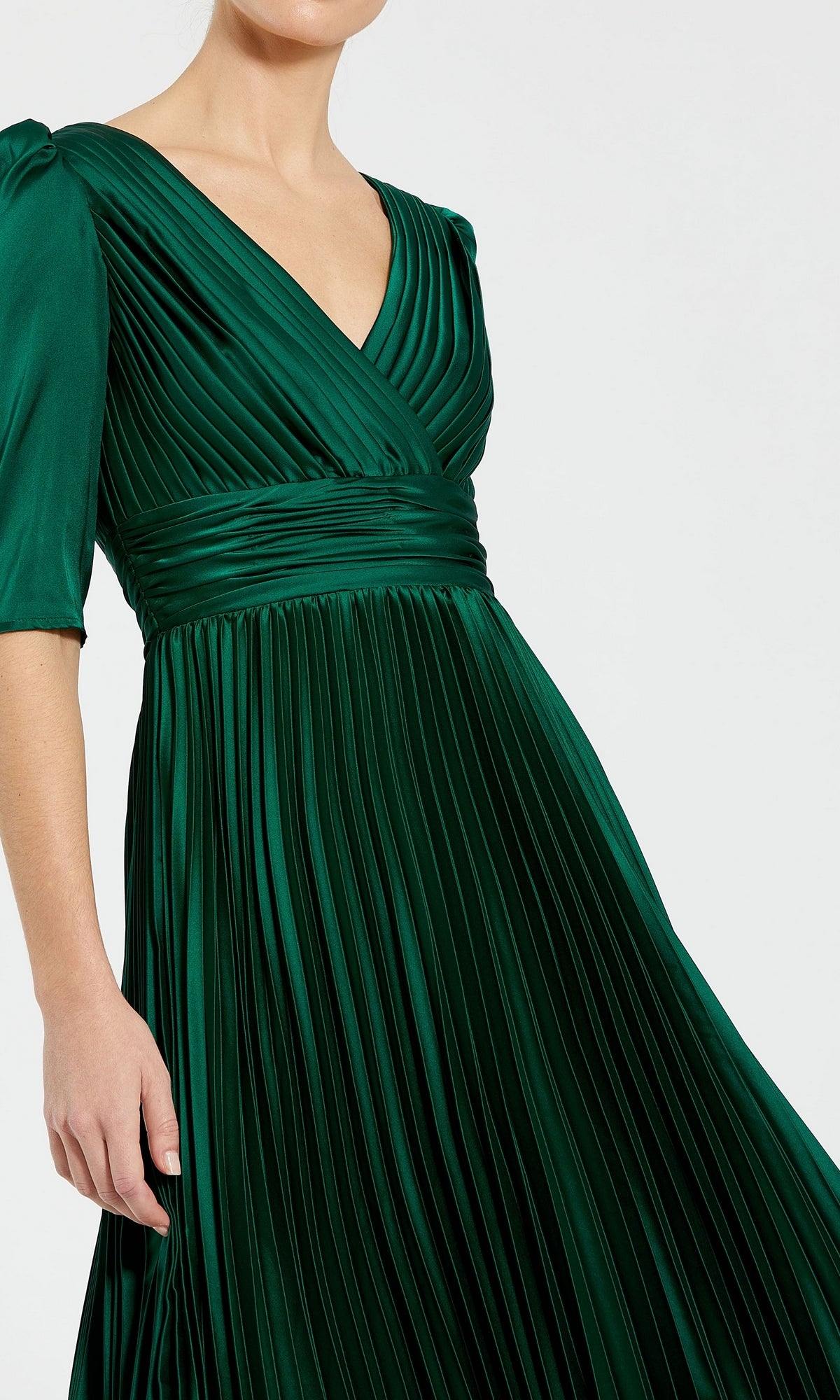 A woman stands against a plain background in the Long Formal Dress 27341 by Mac Duggal—an emerald green, pleated A-line gown with a V-neck, short sleeves, and a fitted waistband.