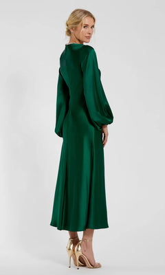 A woman in the Mac Duggal 27350 Modest Midi Wedding Guest Dress in emerald green satin with gold high-heeled sandals stands facing backward, looking over her shoulder.