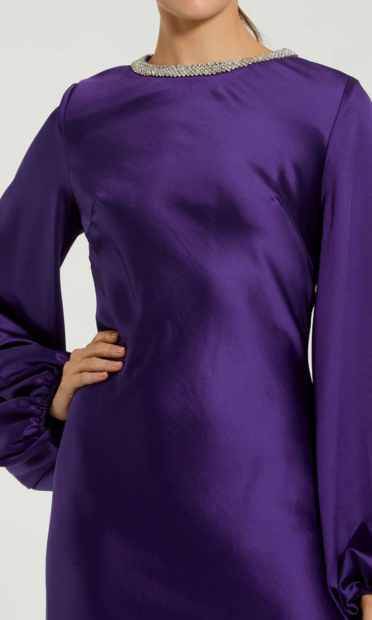 A person in the Modest Midi Wedding Guest Dress: Mac Duggal 27350, featuring long sleeves and a beaded high neckline, stands confidently with one hand on their hip.