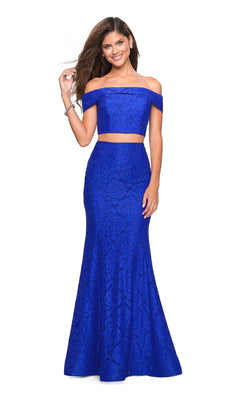 A woman poses in the La Femme Two-Piece Mermaid Lace Prom Dress 27443, featuring royal blue floral lace, off-the-shoulder straps, and a fitted silhouette against a white background.