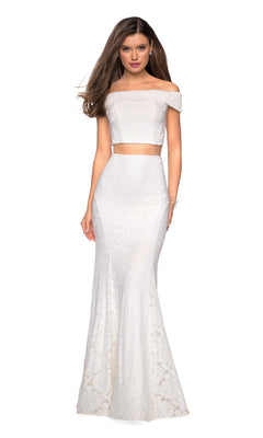 A woman models the La Femme Two-Piece Mermaid Lace Prom Dress 27443, featuring white floral lace, an off-the-shoulder fitted bodice, and a flared mermaid skirt, standing against a white backdrop.