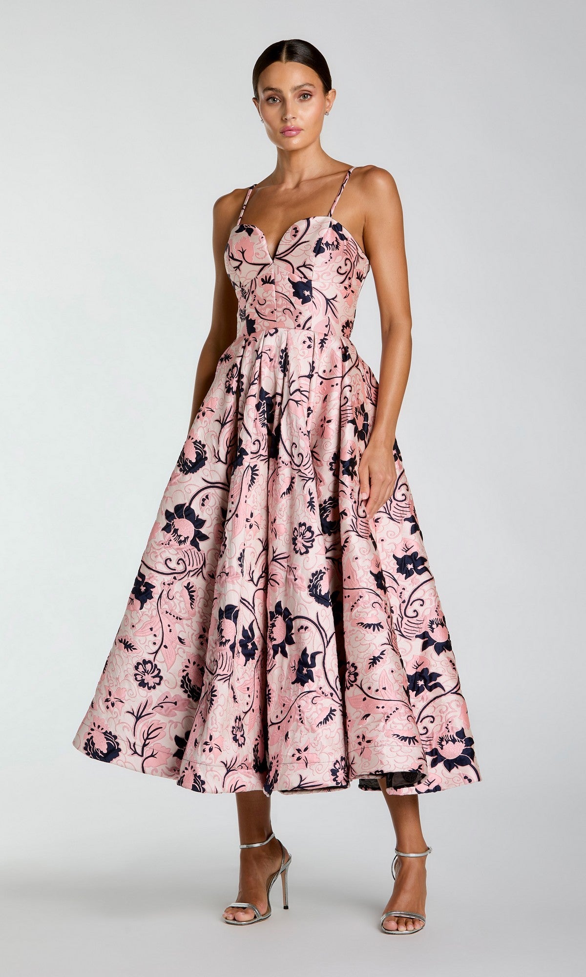 A woman wearing the Mac Duggal 27473 Midi Party Dress in White Multi, featuring a brocade design with a fitted bodice and flared skirt, stands in silver high-heeled sandals against a plain background.