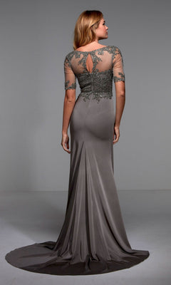 A woman stands facing away from the camera in a plain studio, wearing the Alyce 27477 long formal dress—floor-length, taupe, with an embellished bodice and sheer, embroidered back and sleeves.
