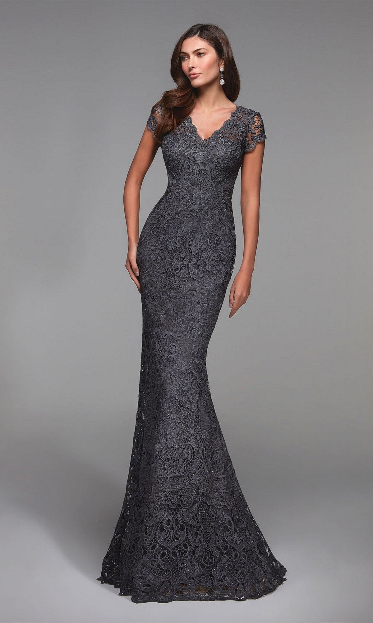 A woman models the Alyce 27478 long formal dress in charcoal, featuring a floor-length, form-fitting lace design with short sleeves and a V-neckline, standing against a plain gray background.