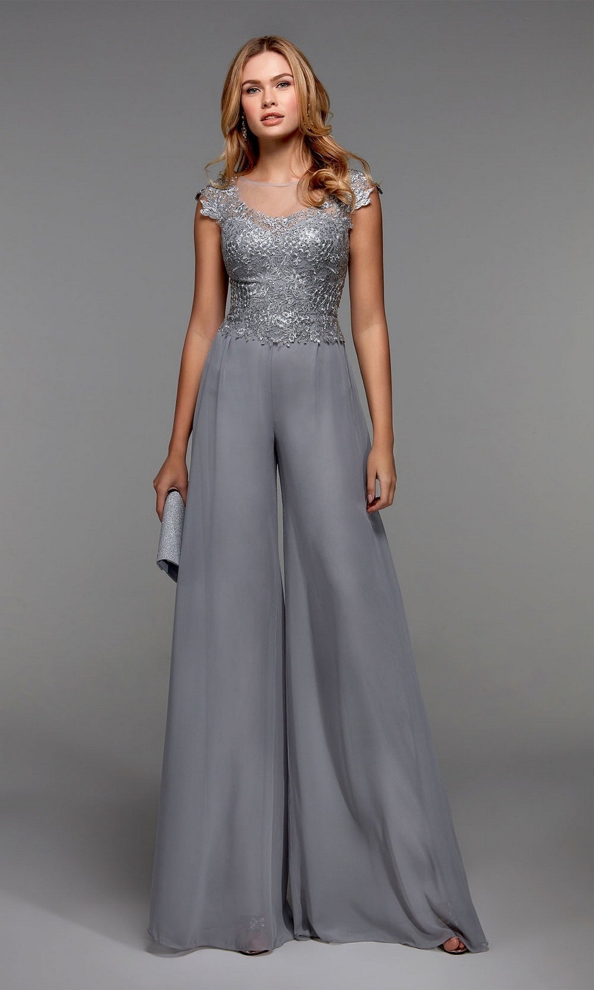 A woman wears the Alyce 27488 long formal jumpsuit in silver, featuring a fitted embroidered bodice, capped sleeves, and flowing chiffon pants, paired with a matching clutch.