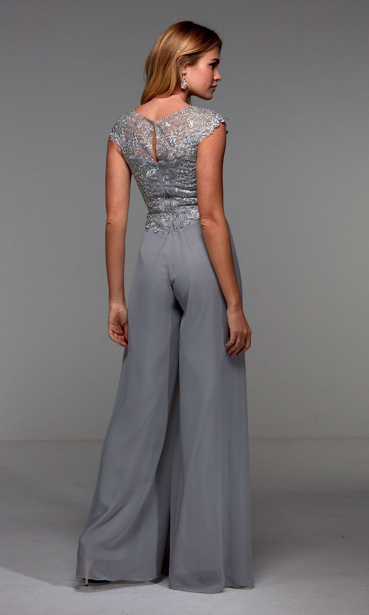 A woman wearing the Alyce 27488 long formal jumpsuit, featuring a silver lace embroidered bodice and wide-leg chiffon pants, stands with her back to the camera in a plain studio setting.
