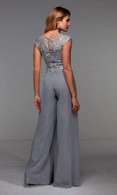 A woman wearing the Alyce 27488 long formal jumpsuit, featuring a silver lace embroidered bodice and wide-leg chiffon pants, stands with her back to the camera in a plain studio setting.