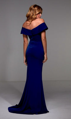 A woman stands facing away in a plain, light-colored room, wearing the Long Formal Dress: Alyce 27489—an off-the-shoulder, floor-length, fitted royal blue gown.