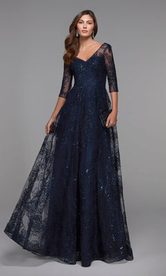 A woman models the Alyce 27494 long navy formal dress, featuring sheer sequin lace sleeves and a V-neckline, standing against a plain gray backdrop.
