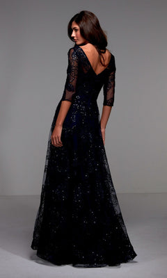 A woman wears the Alyce 27494, a long navy formal dress with sequin lace sleeves and a deep V-back, posing elegantly in a studio—perfect for the mother of the bride.