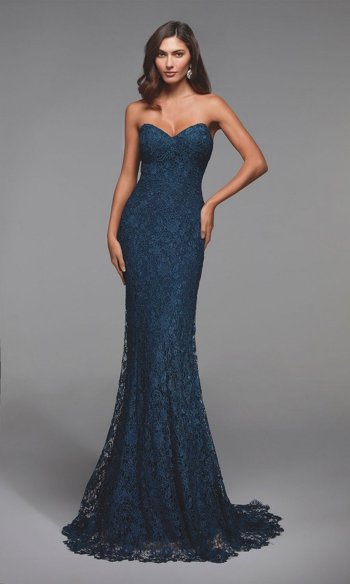 A woman stands against a plain gray background wearing the Alyce 27496, a navy blue, floor-length mermaid formal dress with a strapless neckline and shimmering lace.