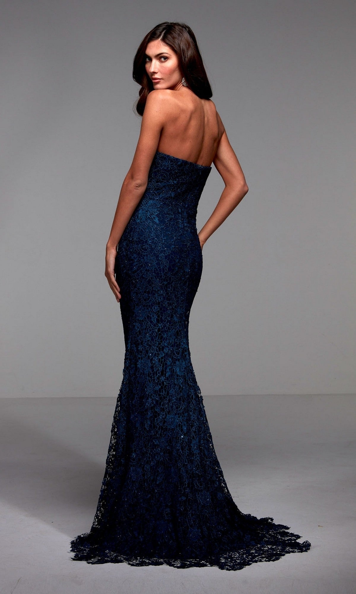 A woman faces away in the Alyce 27496 long formal dress, featuring a strapless neckline, curve-hugging dark blue mermaid silhouette, shimmering lace back detail, and floor-length train against a plain background.