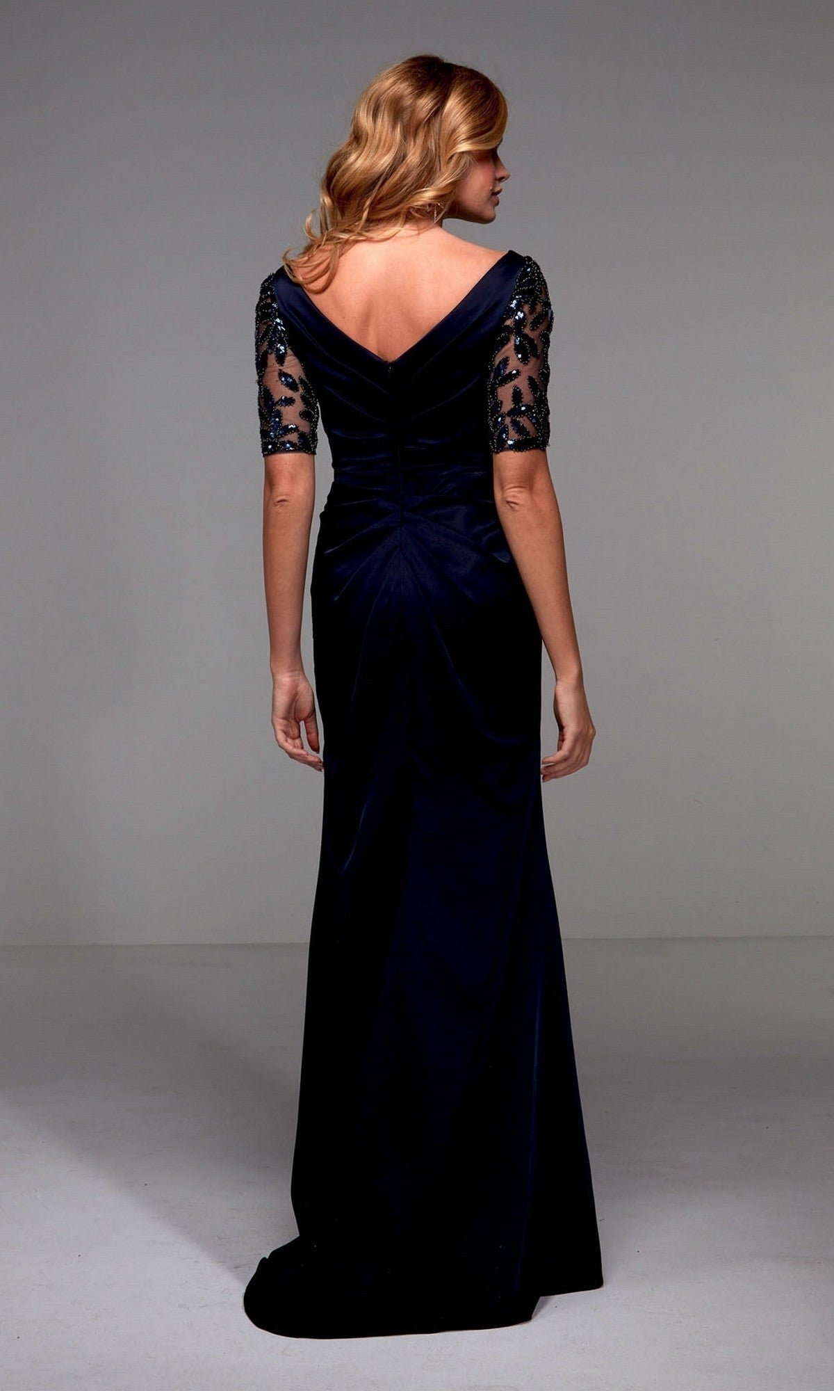 A woman faces away, wearing the Alyce 27498 long formal dress in navy blue with a V-back and elbow-length embroidered lace sleeves—an elegant choice for any formal event.