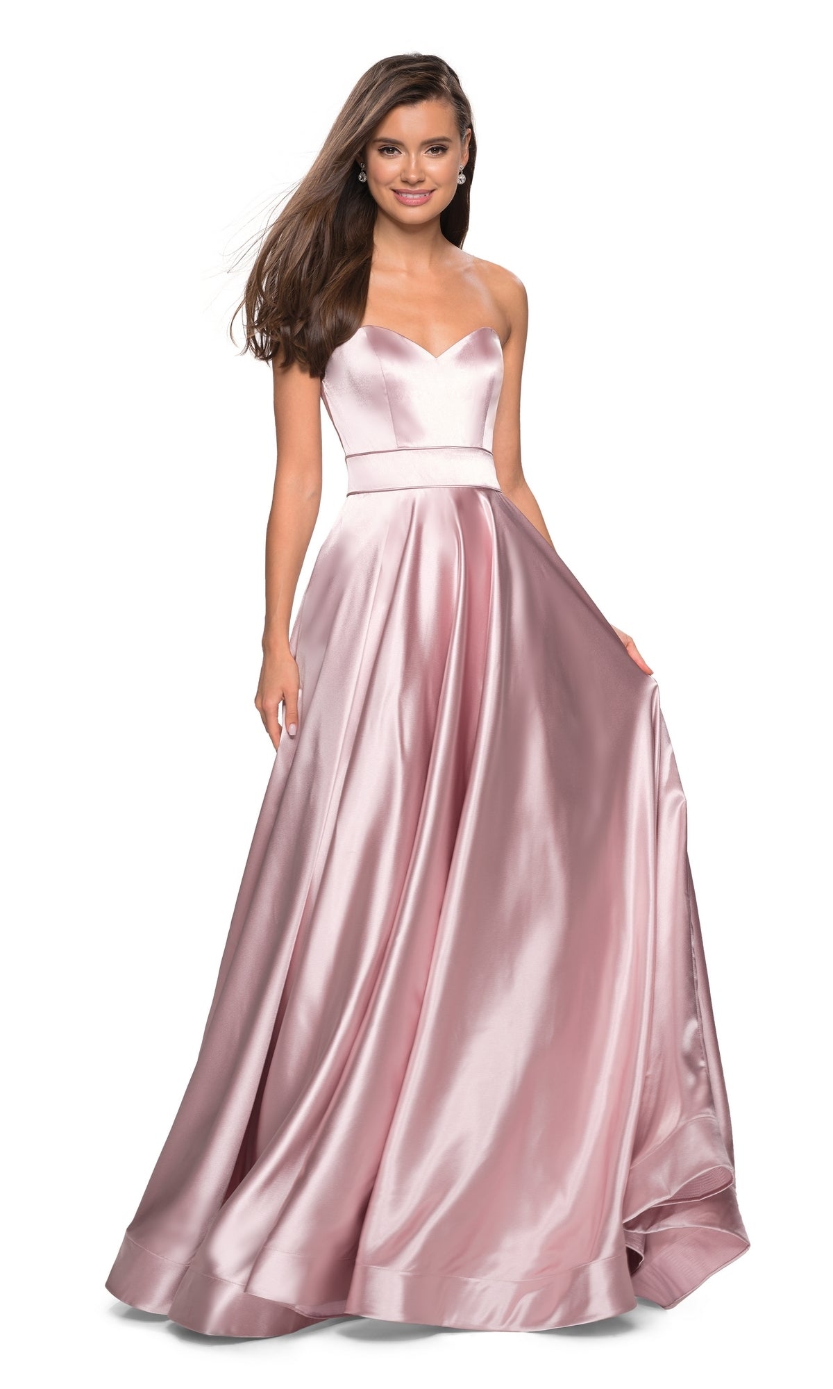 A woman wearing the Strapless A-Line Satin Prom Dress: La Femme 27506 in rose gold, featuring a fitted bodice and full skirt, stands and smiles.