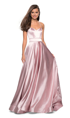 A woman wearing the Strapless A-Line Satin Prom Dress: La Femme 27506 in rose gold, featuring a fitted bodice and full skirt, stands and smiles.