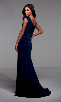 A woman stands in a studio wearing the Alyce 27508, a luxe jersey long formal navy blue mother-of-the-bride dress with cap sleeves, fitted silhouette, and floor-length hem, looking over her shoulder.