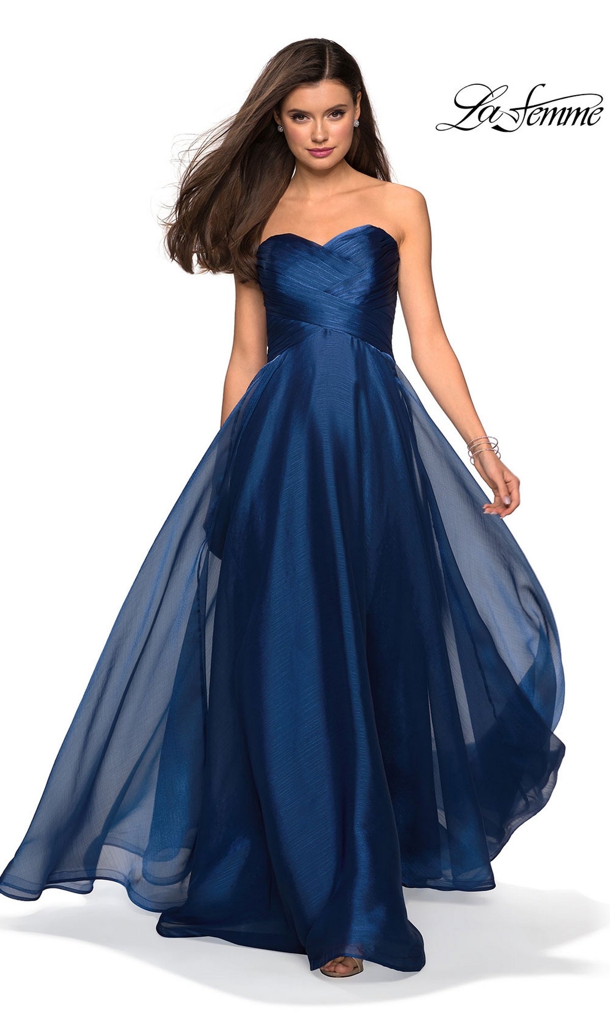 A woman models the La Femme Strapless Long Prom Ball Gown 27515 in navy blue, featuring a flowing sheer overlay and elegant sweetheart bodice, standing against a plain white background.