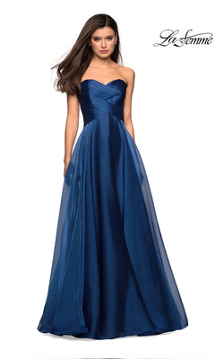 A woman models the La Femme Strapless Long Prom Ball Gown 27515 in navy blue, featuring a fitted bodice and flowing skirt, as she stands against a plain white background.