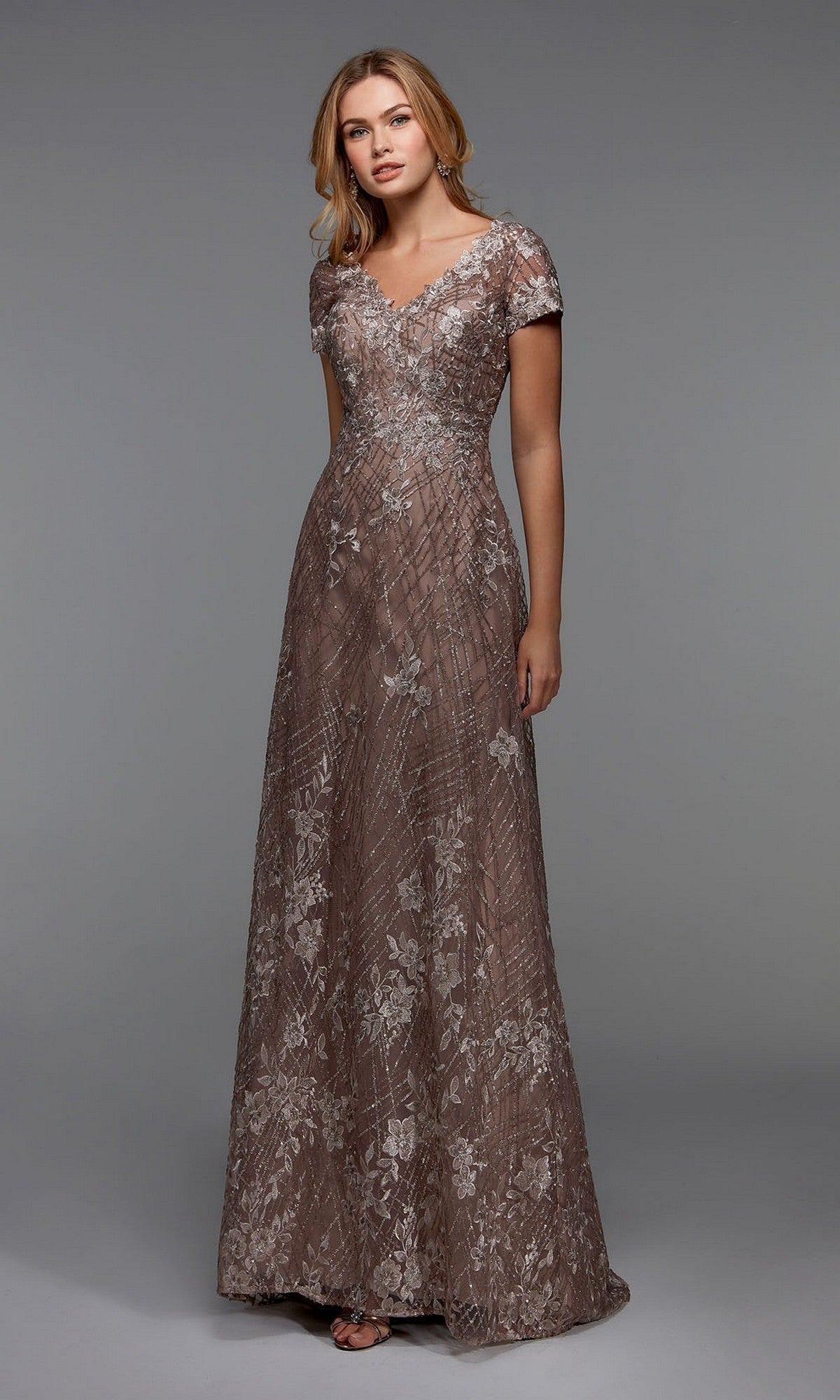 A woman wears the Alyce 27525 long formal dress in shadow grey, featuring short sleeves and silver floral embroidery, standing against a plain gray background.