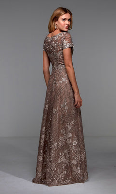 A woman faces away, wearing the Alyce 27525 long formal dress—a floor-length brown gown with short sleeves and floral lace appliques—posed in a simple studio setting.