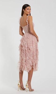A woman stands facing backward with her head turned toward the camera, wearing the Mac Duggal 27529 Midi Party Dress—a light pink dress featuring a ruffled corset bodice, delicate lace detailing, sheer accents, and paired with gold high-heeled sandals.