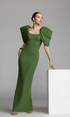 A woman in the Mac Duggal 27534 Puff-Sleeve Long Formal Dress, featuring a fitted green silhouette and large puffed sleeves, stands beside a white rectangular block against a plain gray background.