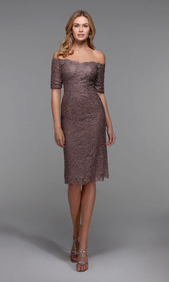 A woman wearing the Alyce 27535 Knee Length Semi-Formal Dress in Smoke, featuring an off-the-shoulder lace sheath design, paired with silver strappy heels, stands against a plain gray background.