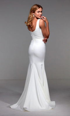 A woman wearing the Alyce 27538 long white dress, featuring a sleeveless fitted bodice, crystal-embellished neckline, and flared skirt, stands looking over her shoulder.