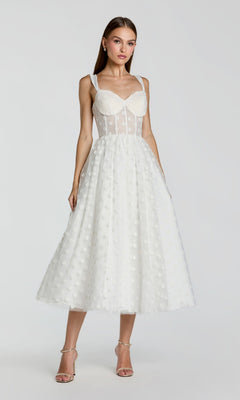 A woman models the Mac Duggal 27539 Black Midi Polka Dot Party Dress featuring a fitted bodice and sheer panels, paired with neutral heels, against a plain background.