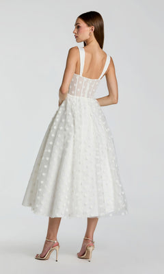A woman seen from behind wears the Mac Duggal 27539 Black Midi Polka Dot Party Dress, featuring a sleeveless design, wide straps, tea-length sheer overlay, and paired with high-heeled sandals.