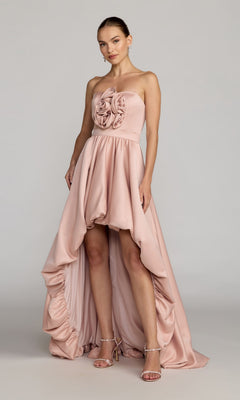 A woman wearing the Mac Duggal 27554 High-Low Formal Dress in blush, featuring a strapless bodice adorned with ruffled, rose-inspired details, elegantly paired with strappy heels.