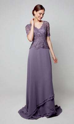 A woman in the Alyce 27556 long formal dress in hydrangea, featuring a beaded lace bodice and short sleeves, stands against a plain light background, looking down with one hand touching her neck.