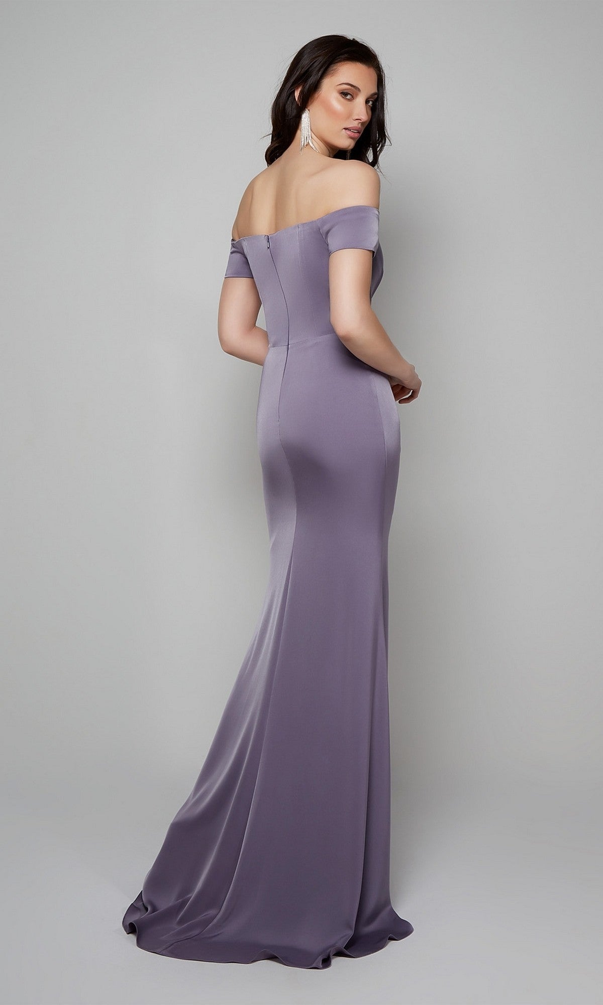 A woman poses against a light background, looking back over her shoulder while wearing the Alyce 27558—a floor-length, lavender, off-the-shoulder formal dress styled like a fitted sheath evening gown.