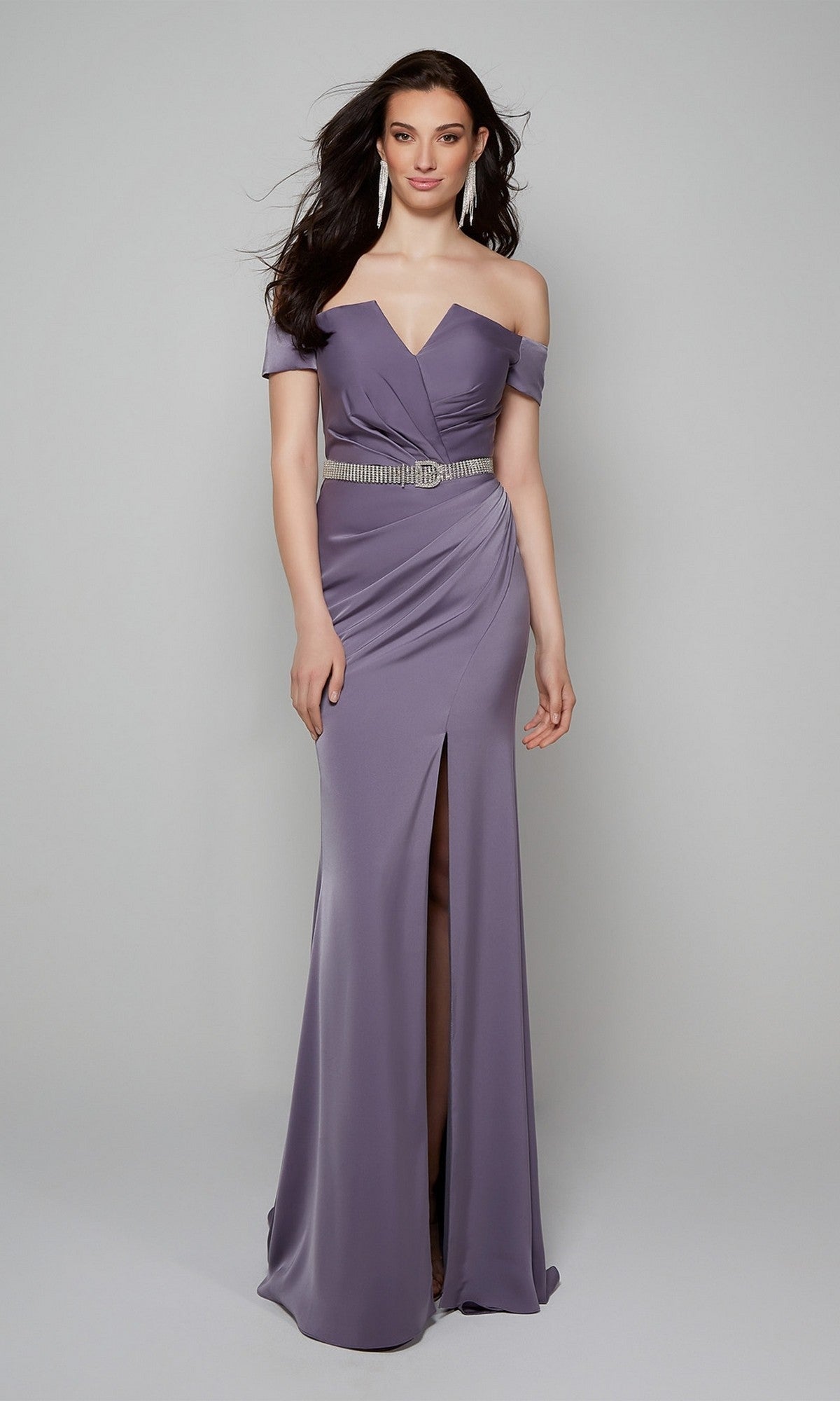 A woman models the Alyce 27558 long formal dress—an off-the-shoulder lavender gown with a thigh-high slit and silver belt—showcasing chic mother of the bride style against a plain light gray background.